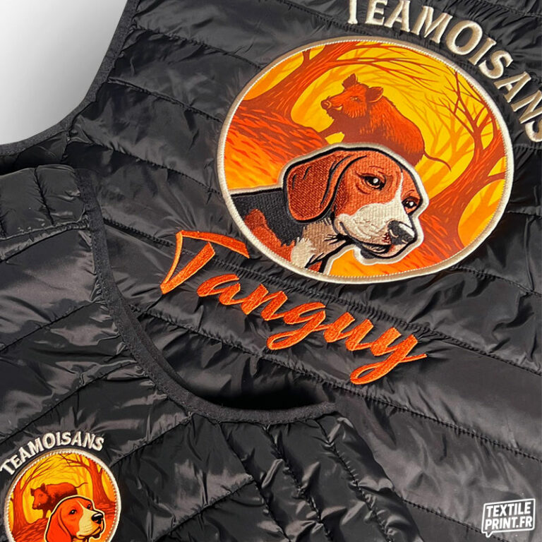 Zoom sur la broderie personnalisée d’une doudoune sans manches K6113/K6114 : logo Team Oisans Copains Chasseurs avec chien et sanglier, prénom Tanguy – réalisation Textile-Print