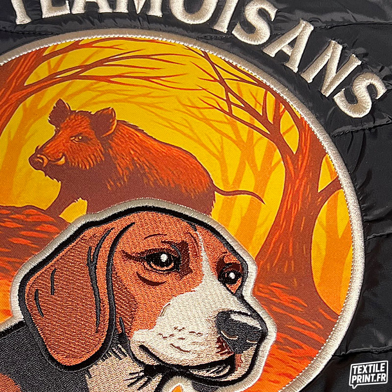 Zoom sur le logo Team Oisans Copains Chasseurs brodé avec applique sur doudoune sans manches K6113/K6114 – chien et sanglier en broderie haute qualité par Textile-Print