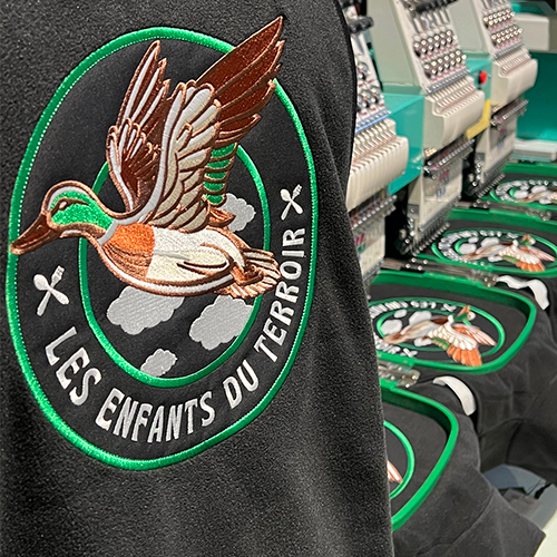 Broderie Les Enfants du Terroir en cours de production sur bodywarmers polaires recyclés – atelier textile professionnel.