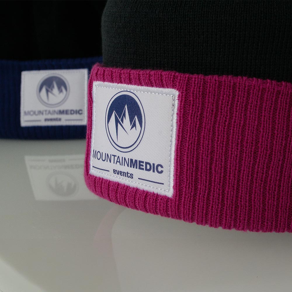 Zoom sur l’écusson brodé MountainMedic cousu sur le revers d’un bonnet rose et bleuté.