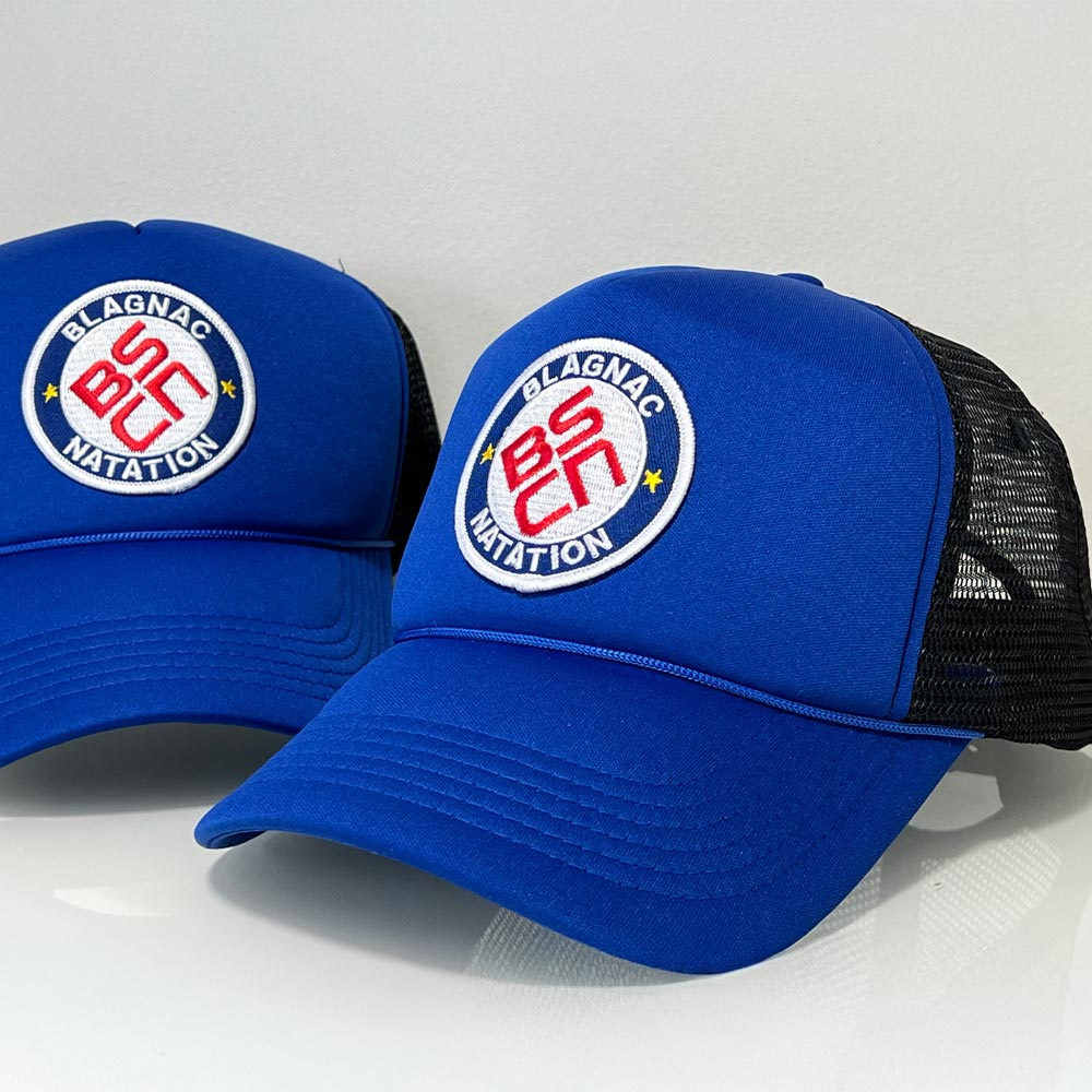 Deux casquettes personnalisées bleu roi Blagnac Natation avec écusson brodé, posées sur surface blanche.