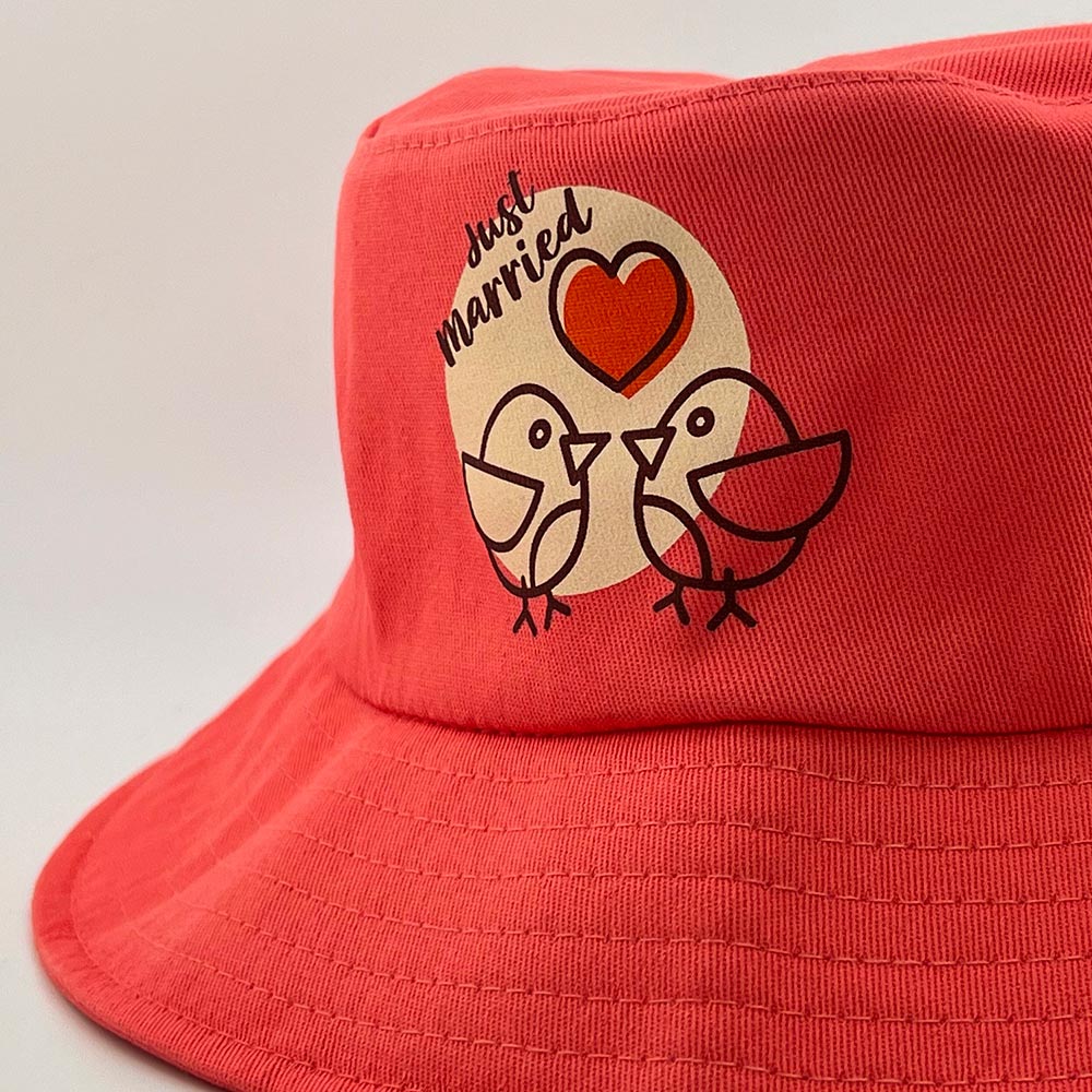 Zoom sur le motif Just Married imprimé sur un bob rose, représentant deux oiseaux et un cœur.