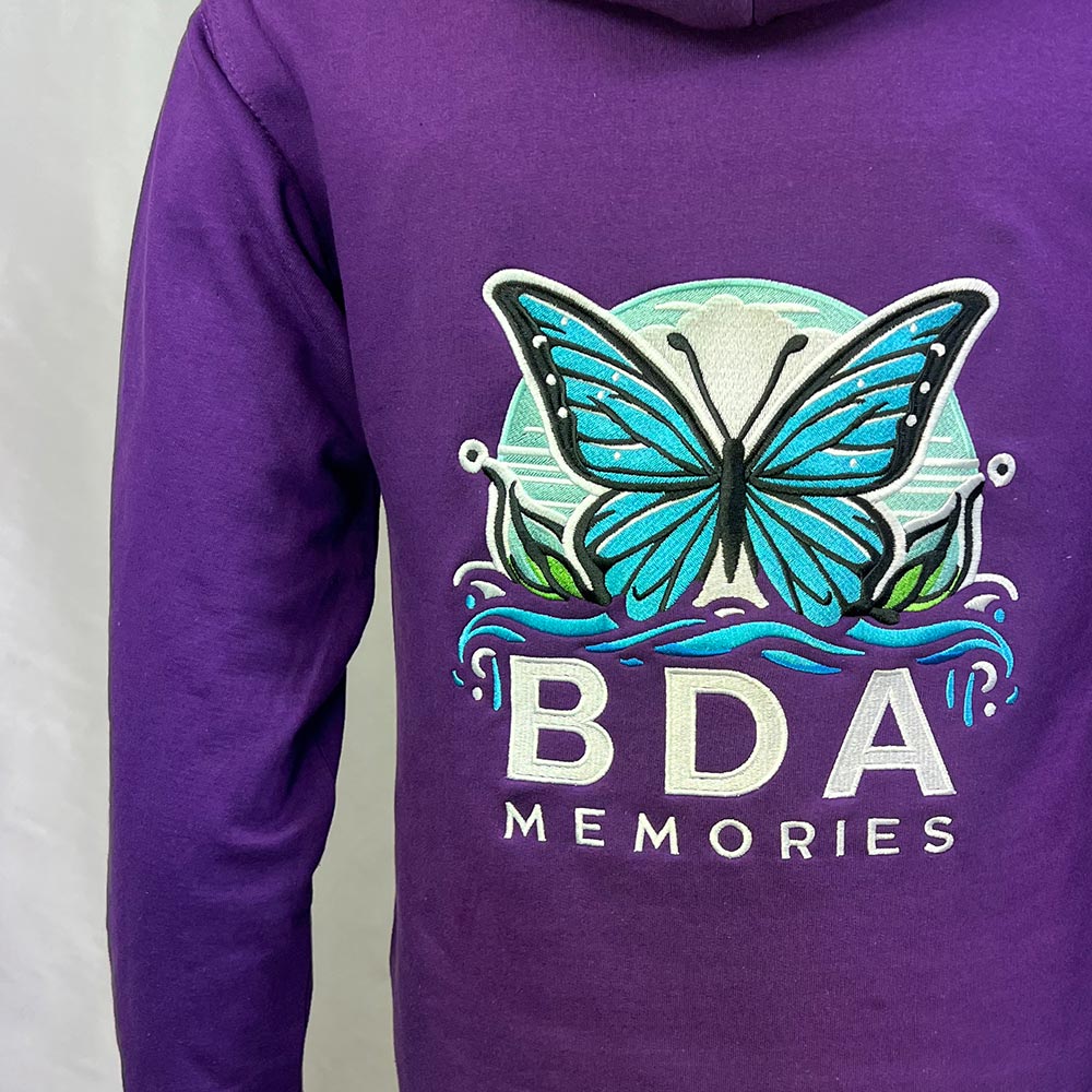 Broderie papillon BDA Memories sur le dos d’un sweat violet, vue rapprochée.