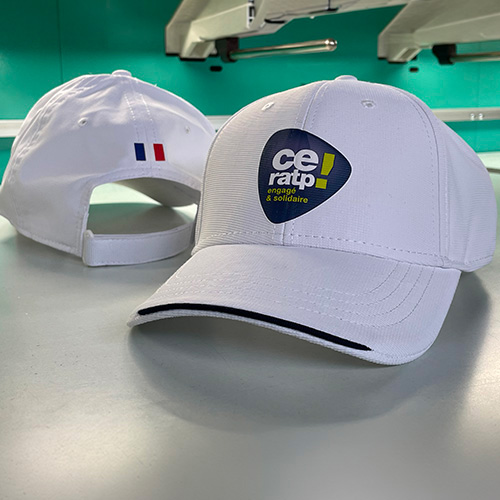 Deux casquettes blanches personnalisées avec le logo CE RATP posées sur une table.